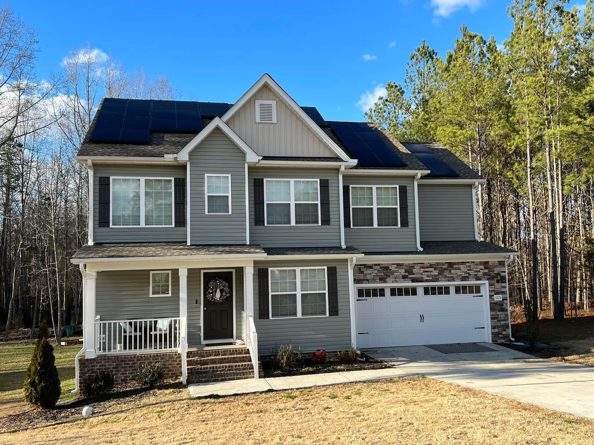 Two-story suburban gray siding home with dark solar panels surrounded by trees